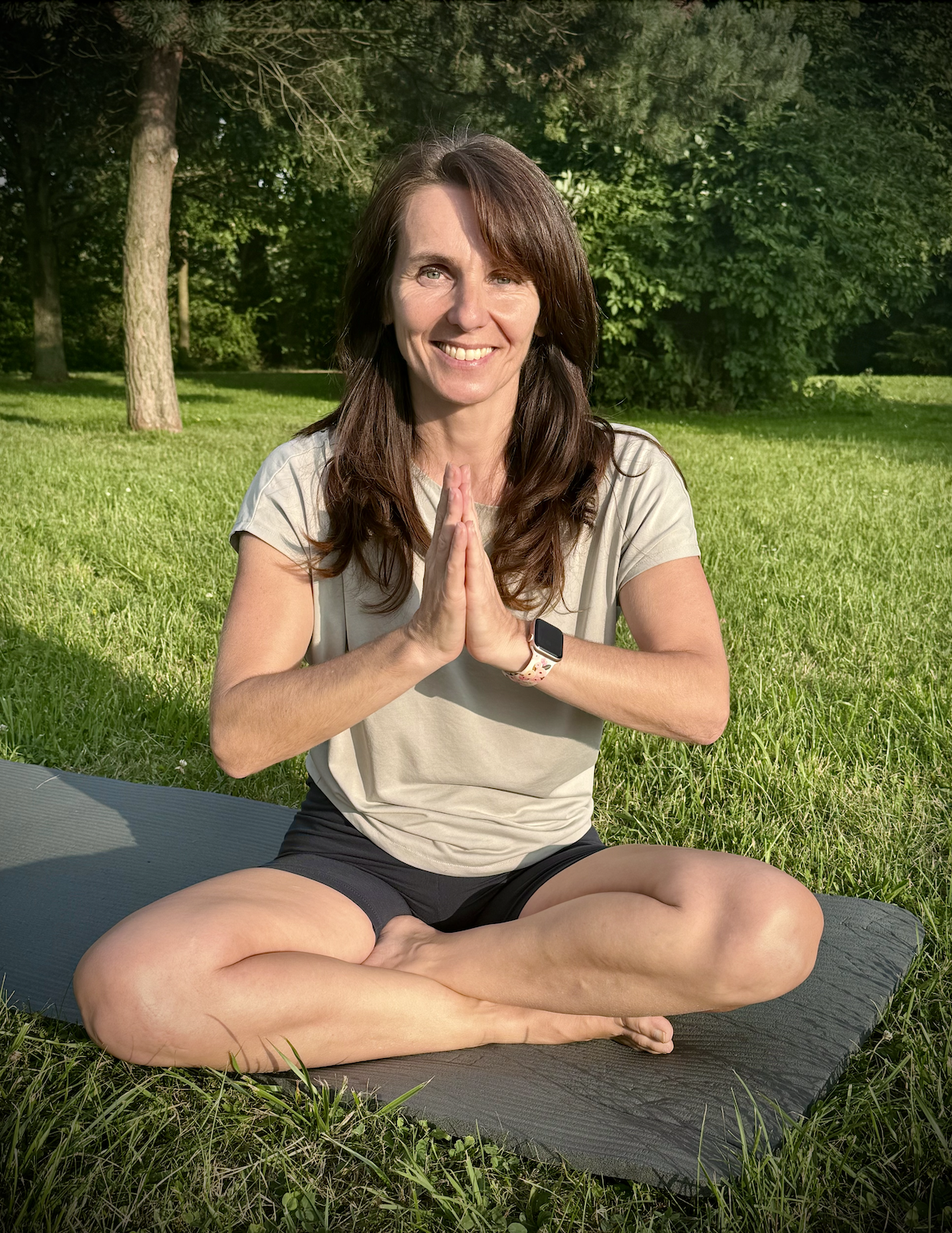 Marketa looking into the camera while seated in lotus on the grass, hands together